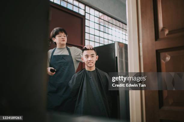 an asian chinese mid adult woman is cutting and trimming hair for her son in the kitchen due to travel ban - teenage boy shave imagens e fotografias de stock