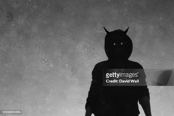 a scary, hooded horned figure with glowing evil eyes looking down to camera. with a grainy textured edit - teufel stock-fotos und bilder