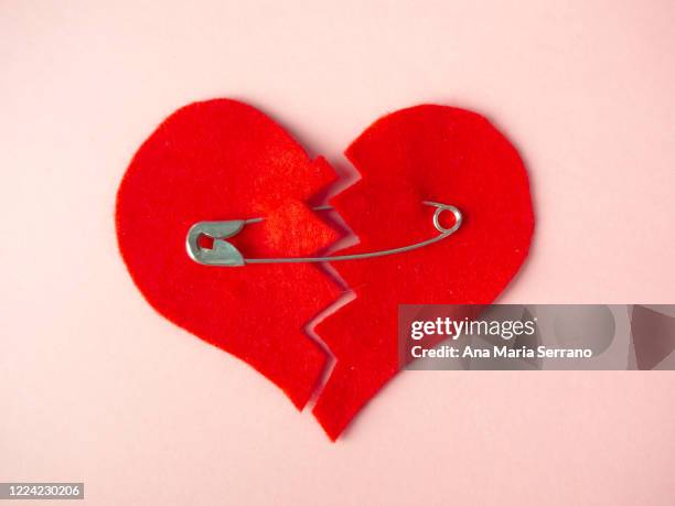 a broken heart sewn with safety pins against pink background. heartbreak concept - affairs stockfoto's en -beelden