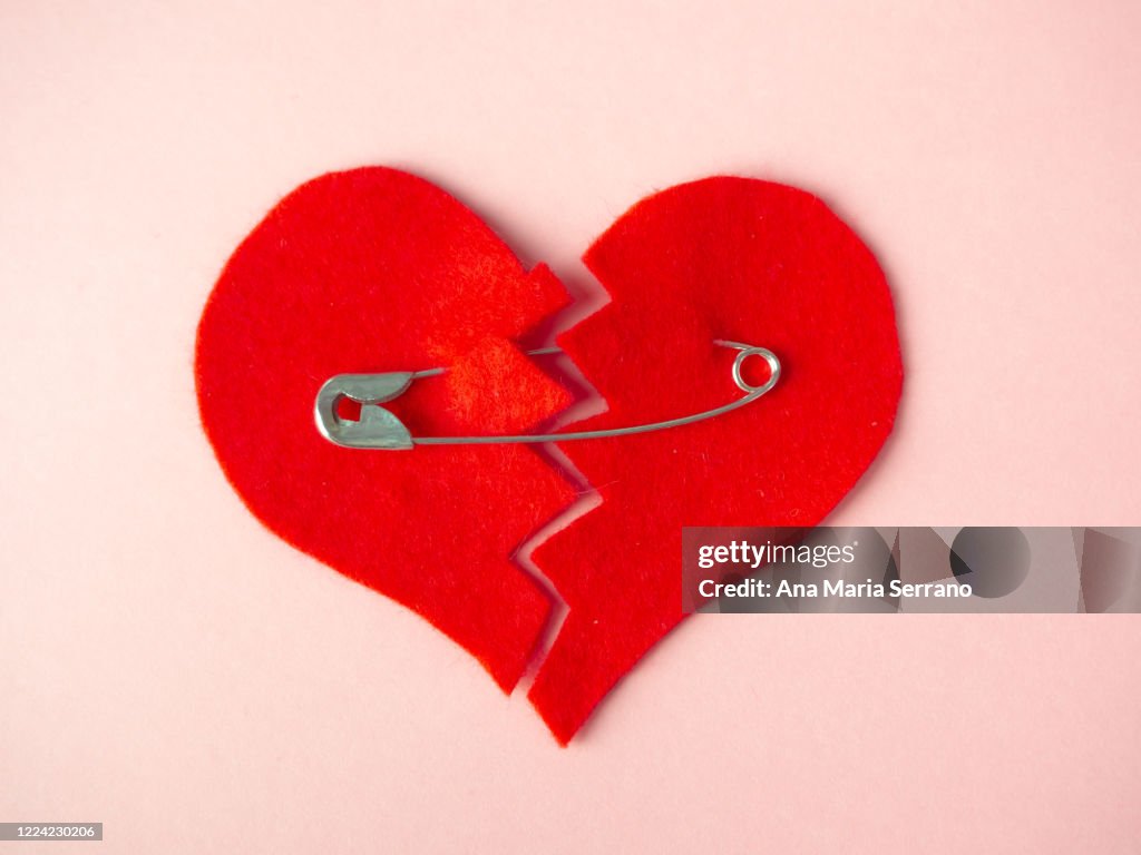 A broken heart sewn with safety pins against pink background. Heartbreak concept