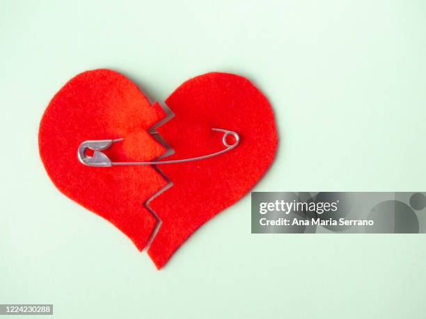 a broken heart sewn with safety pins against green background. heartbreak concept - hearts playing card foto e immagini stock