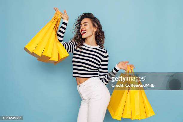 conceptual photo of happy girl holds shopping packages on blue background - buying stock pictures, royalty-free photos & images