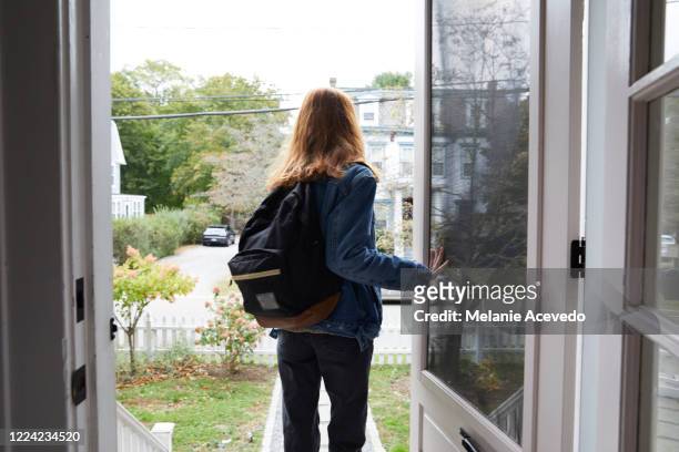 teenage girl walking out the front door of her house. back view of her leaving the house. she is on her way to school, wearing a back pack and holding the door open. - leaving stock-fotos und bilder