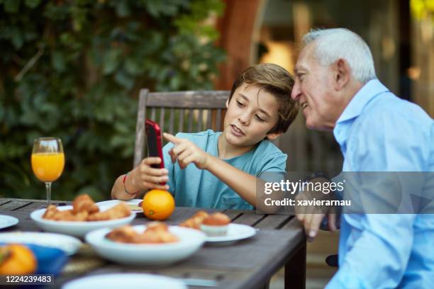 young boy educating grandfather about smart phone features - pensioners demonstrate in spain stock pictures, royalty-free photos & images