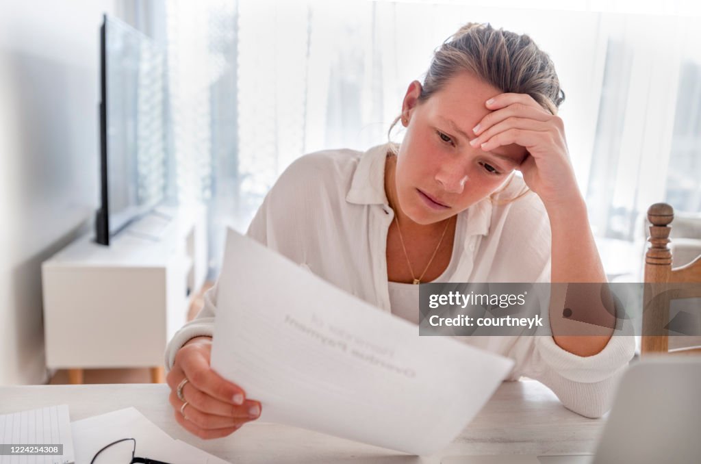 Woman looking worried holding paperwork at home.