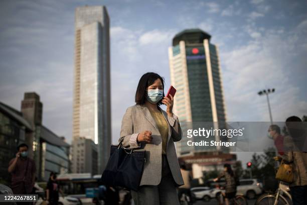 Women wears a mask while uses iPhone pass the crossroads on May 11, 2020 in Wuhan, China. The government has begun lifting outbound travel...