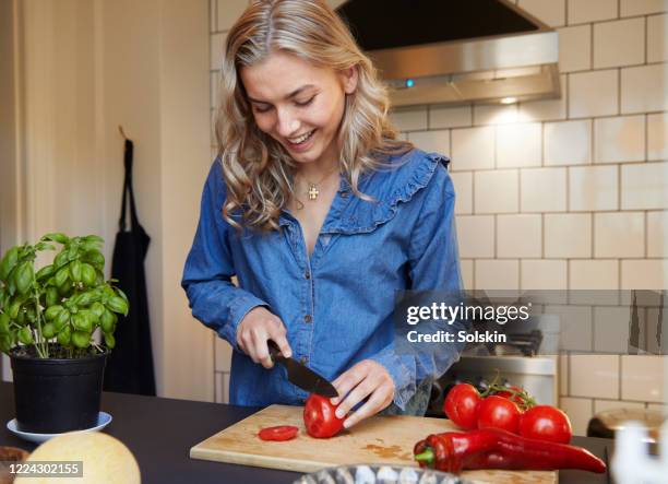 young woman in kitchen preparing vegetables - doorknippen stockfoto's en -beelden