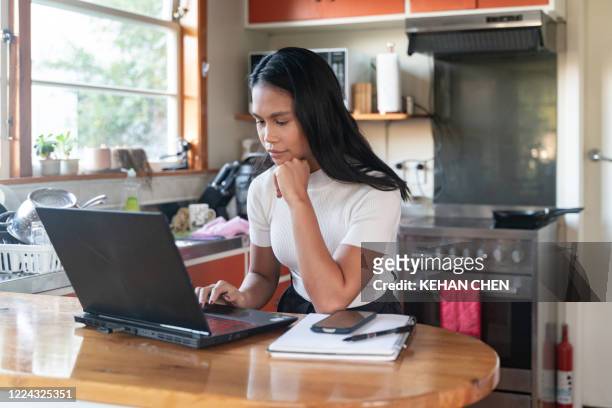 asian businesswoman working from home during covid-19 lockdown using laptop in kitchen - auckland covid stock pictures, royalty-free photos & images