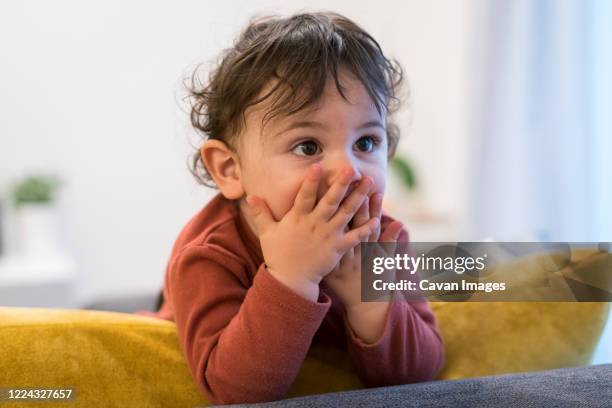 baby boy covering mouth and looking away while standing on sofa - covering nose stock pictures, royalty-free photos & images