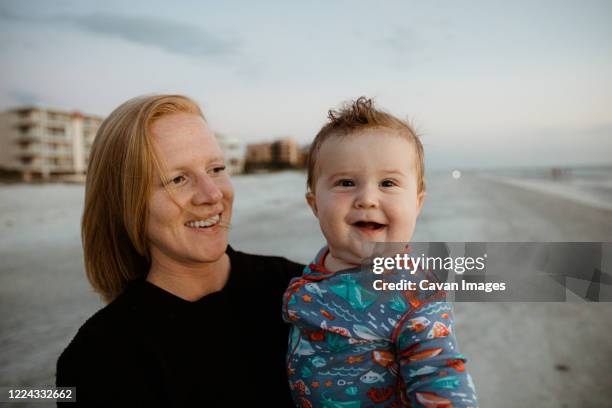 fat baby boy with crooked smile held by young red haired mom on beach - chubby girls stock pictures, royalty-free photos & images