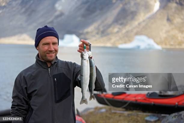 man holding up fresh arctic char in greenland - char stock pictures, royalty-free photos & images