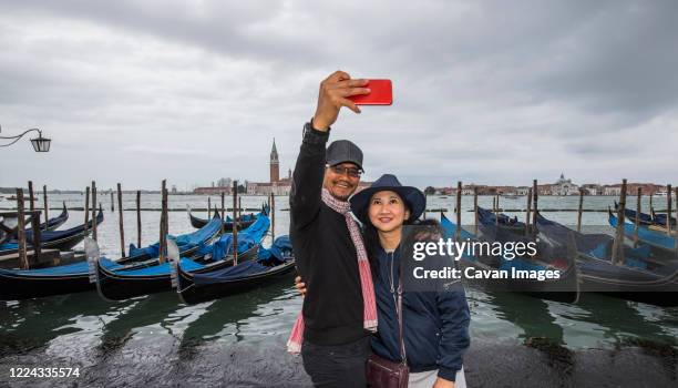 thai couple taking selfie in front of parked gondola's in venice - gondola traditional boat stockfoto's en -beelden