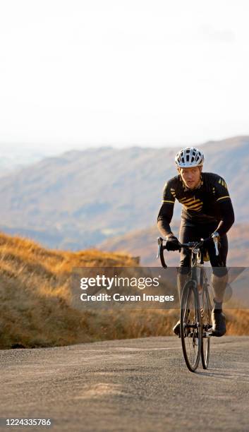 cyclist approaching top of hill in the british lake district - road cycling stock pictures, royalty-free photos & images