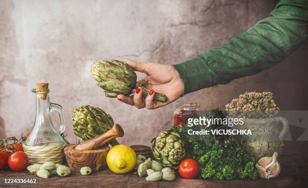 woman hand with artichoke and ingredients of mediterranean cuisine - mediterranean culture stock pictures, royalty-free photos & images