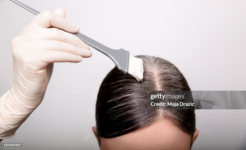 Frau färbt graue Haarwurzel mit Pinsel und Haarfarbe, Nahaufnahme