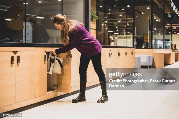 a woman putting her laptop bag in a locker / cabinet in a workspace - spind stock-fotos und bilder