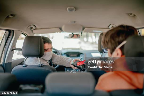 contactless payment for taxi during an illness epidemic. taxi driver and his passenger wearing protective masks and gloves - uber driver stock pictures, royalty-free photos & images