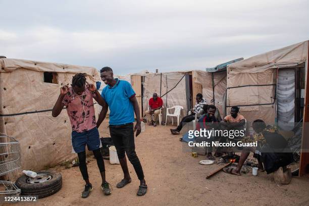 Two migrants pose in a shanty town while other men take tea in front of their 'chabolas' on May 06, 2020 in Lepe, Spain. This shantytown was started...