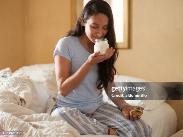 latijnse vrouw in bed dat een kruik van lotion ruikt - smell stockfoto's en -beelden