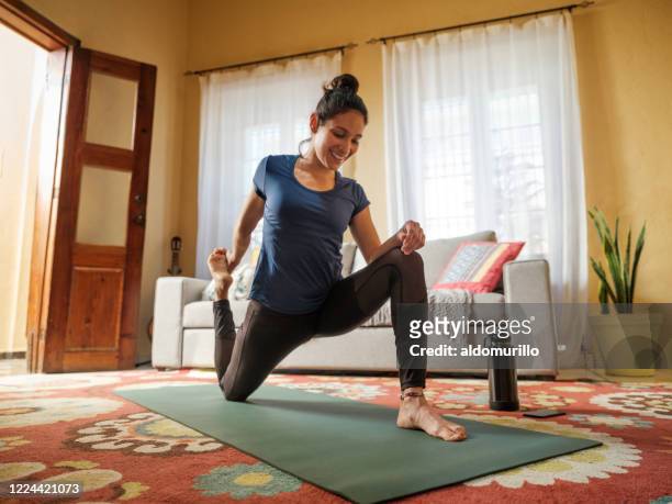 Happy latin woman stretching legs on mat in living room