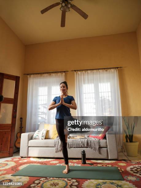 latin woman doing yoga on mat in living room - plastic free stock pictures, royalty-free photos & images