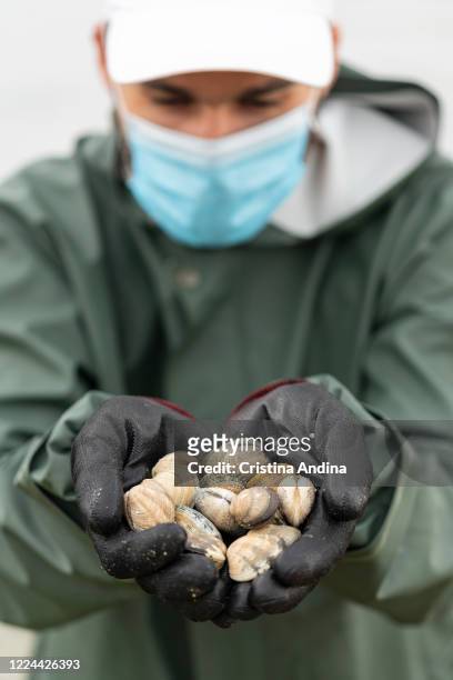 Shellfisherman Adrián González, wearing a surgical mask, shows the photographer the first clams he collects on May 12, 2020 in A Pobra do Caramiñal,...