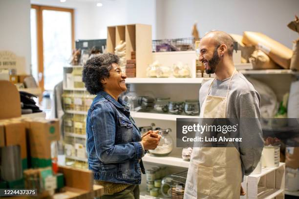 smiling owner and customer laughing at illuminated zero waste store - abrigo blanco artículo de moda fotografías e imágenes de stock