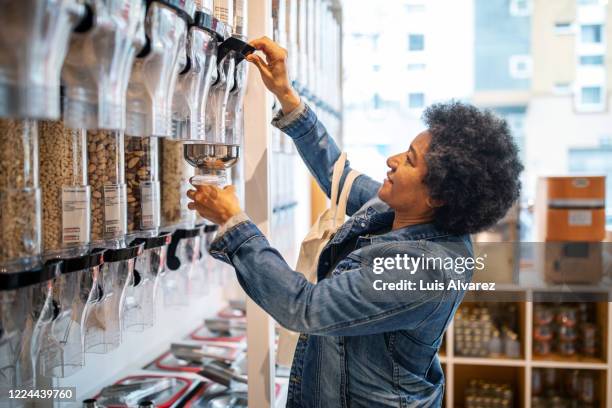 side view of woman filling jar from container at zero waste store - selbstbedienung stock-fotos und bilder