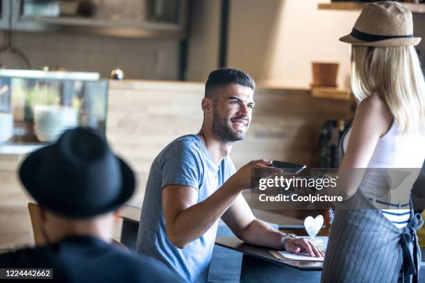 waiter with customer in a hipster café. - customers pay with contactless cards imagens e fotografias de stock
