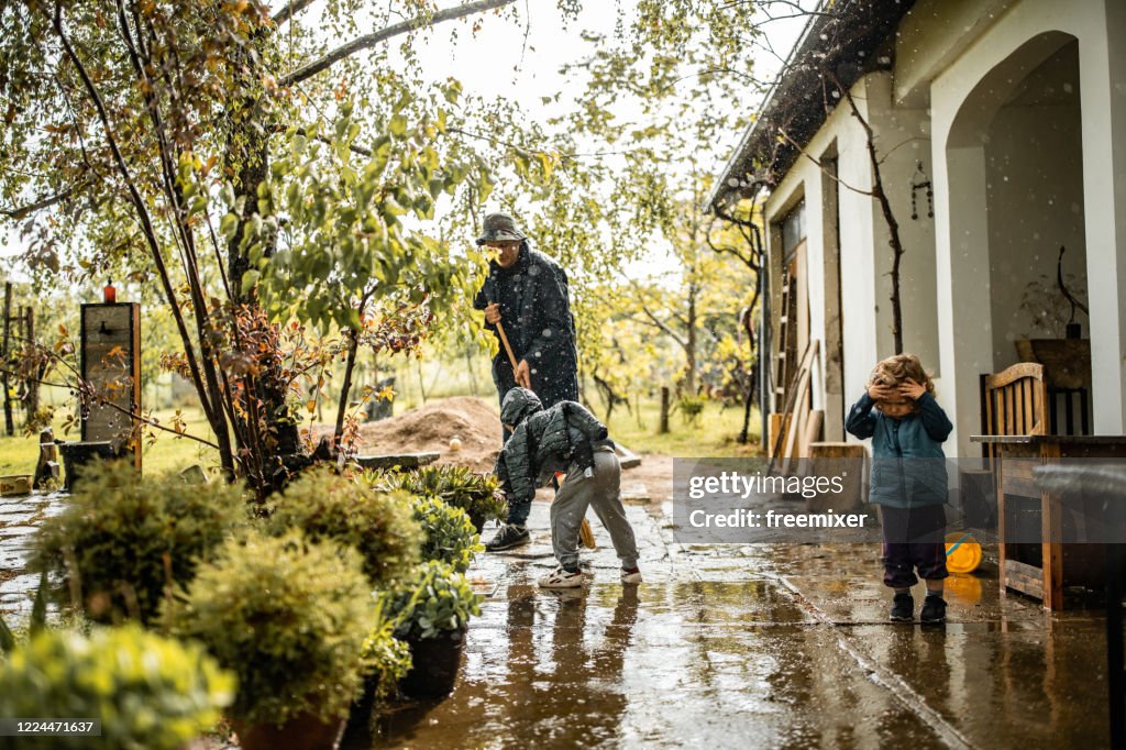 Hijo ayudando al padre y barriendo el agua del patio delantero en el día lluvioso