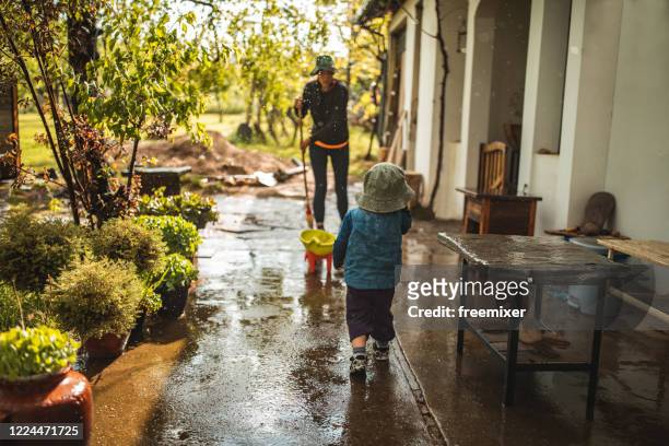 young woman sweeping water from front yard on rainy day - rain garden stock pictures, royalty-free photos & images