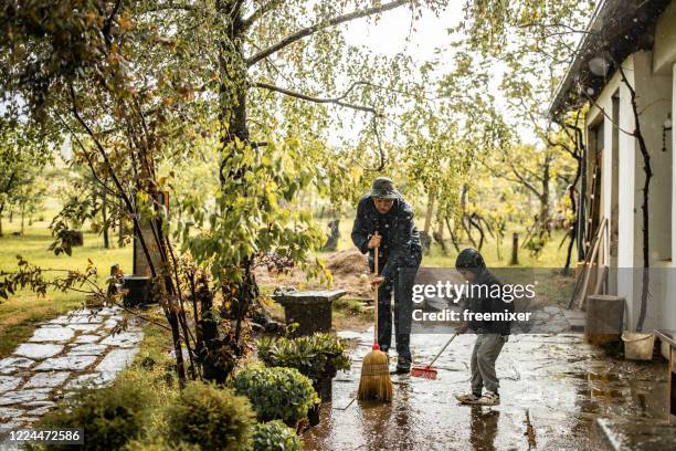 vater und sohn fegen wasseraus vor dem vorgarten am regnerischen tag - flooded home stock-fotos und bilder