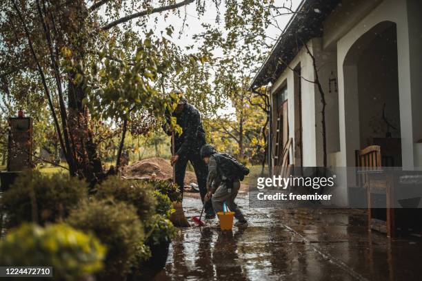 vater und sohn fegen wasseraus vor dem vorgarten am regnerischen tag - flooded home stock-fotos und bilder