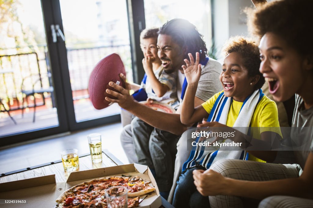 Fröhliche schwarze Familie jubeln, während Rugby-Spiel im Fernsehen zu Hause zu sehen.