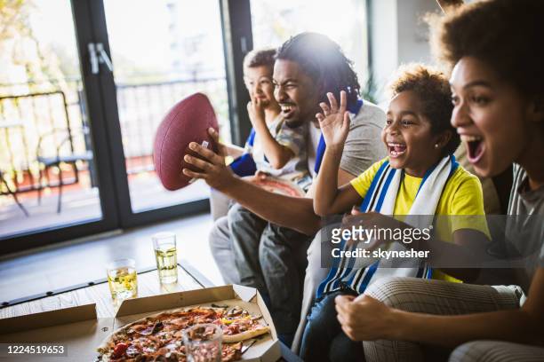 fröhliche schwarze familie jubeln, während rugby-spiel im fernsehen zu hause zu sehen. - match sport stock-fotos und bilder