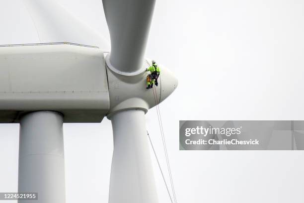 los técnicos de acceso a cuerdas se aletean hasta trabajar en la hoja del aerogenerador y preparar protectores de cuerda en la cuerda. - aerogenerador fotografías e imágenes de stock