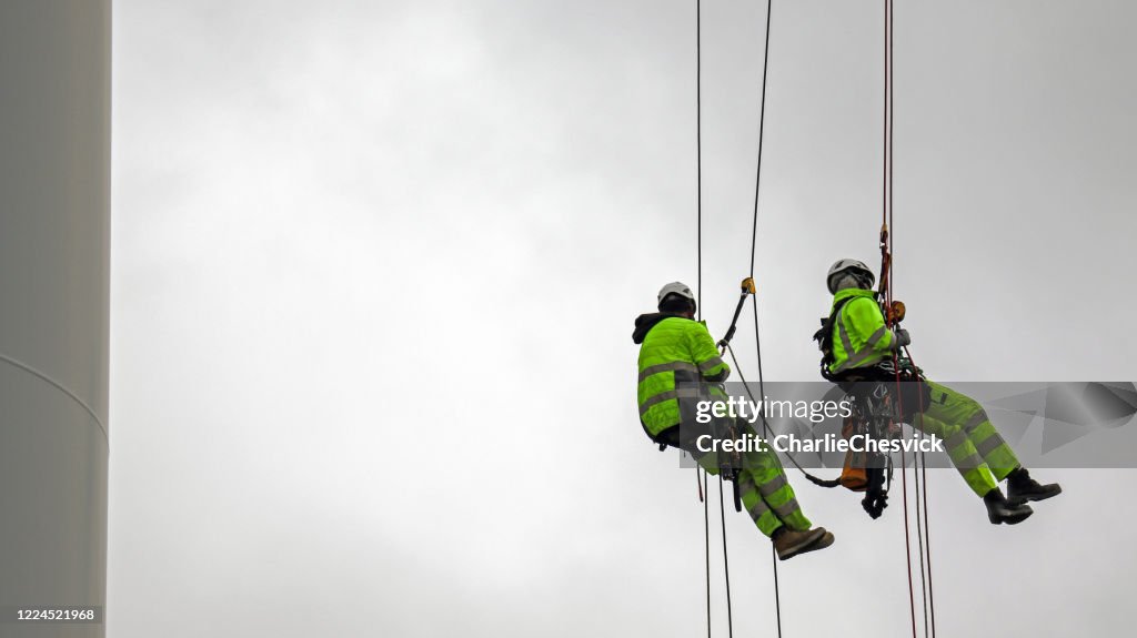 Two rope access technicians rappelling down from blade of wind turbine and they are high up