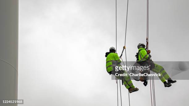 two rope access technicians rappelling down from blade of wind turbine and they are high up - high up stock pictures, royalty-free photos & images