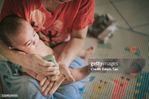 eine asiatische chinesische großmutter anwendung lotion für ihre 5 monate alten baby junge enkel nach dem bad auf matte - baby bath stock-fotos und bilder