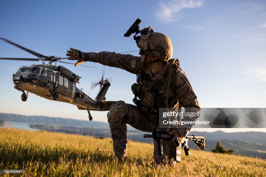 軍用直升機接近跪著的陸軍士兵後面