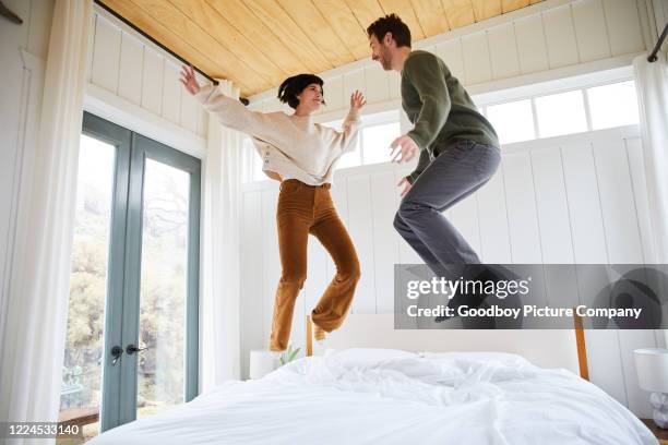 pareja joven despreocupada saltando en su cama en la mañana - mujer saltando en cama fotografías e imágenes de stock