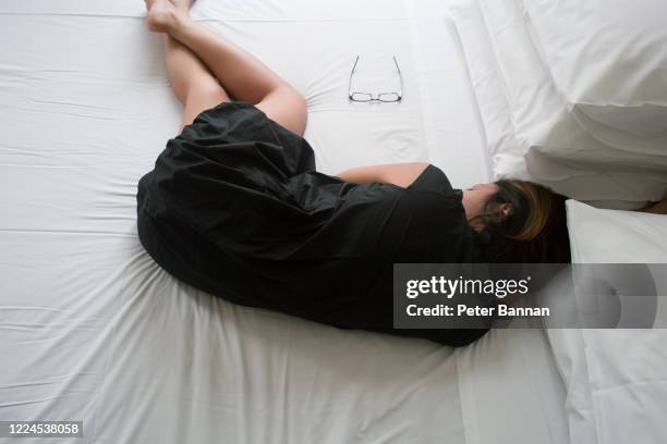 asian woman lying on bed, back view, curled up, wearing black dress - woman curled up stock pictures, royalty-free photos & images