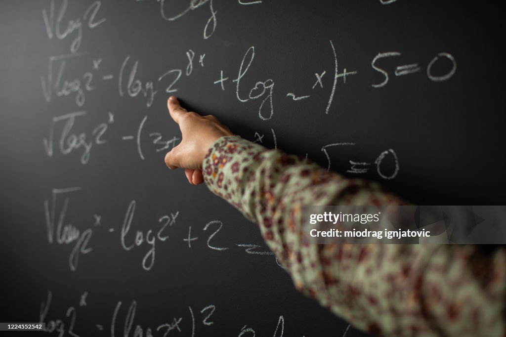 Math teacher showing solution for math problem on blackboard