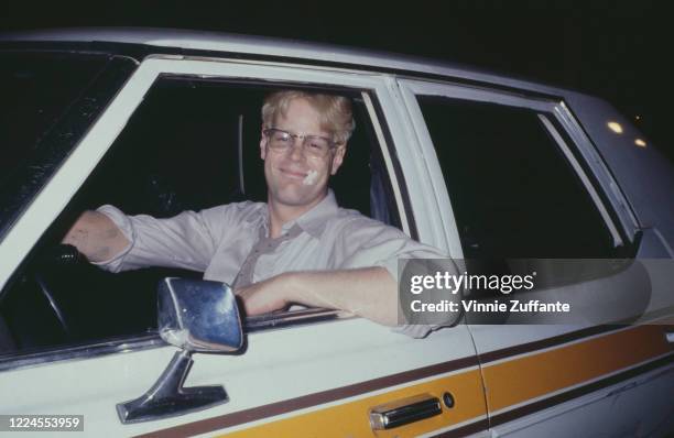 Canadian actor and comedian Dan Aykroyd, with blond hair, as he sits in a car, his elbow resting on the open window of the door, circa 1981.