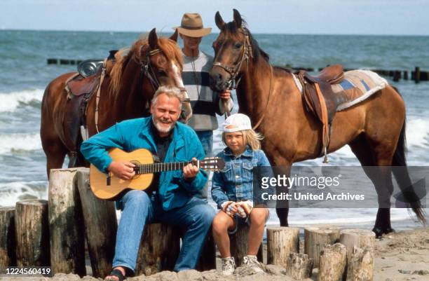 German singer and presenter playing the guitar at the beach with a girl and horses, Germany, circa 1994.