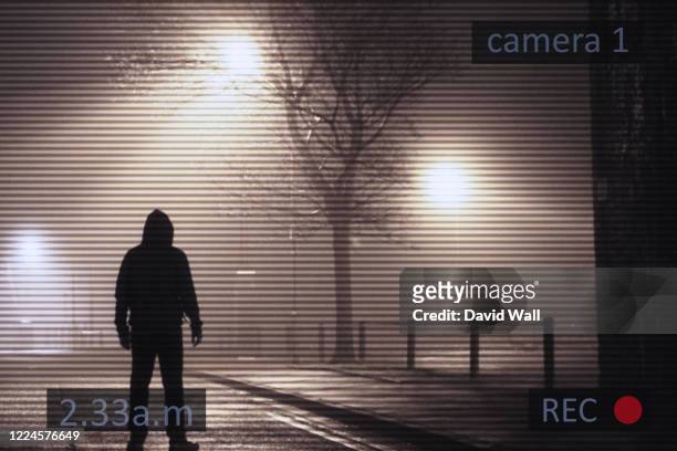 a scary hooded figure standing next to street lights on a foggy winters night. with a cctv surveillance edit. - crime in the uk stock pictures, royalty-free photos & images