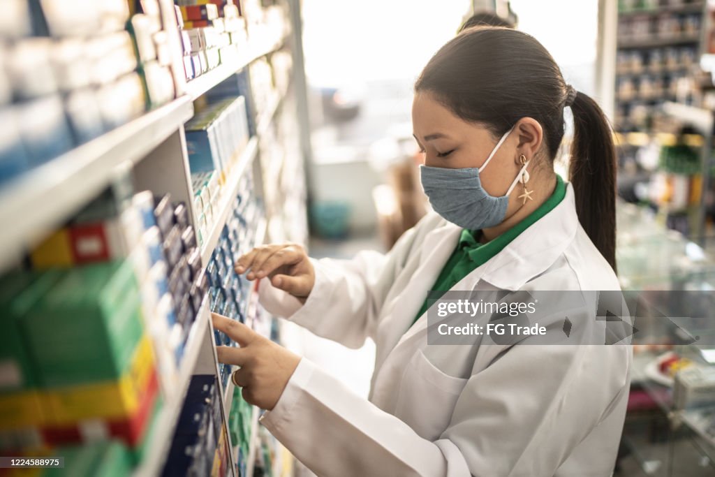 Female pharmacist picking some drugs with face mask at pharmacy