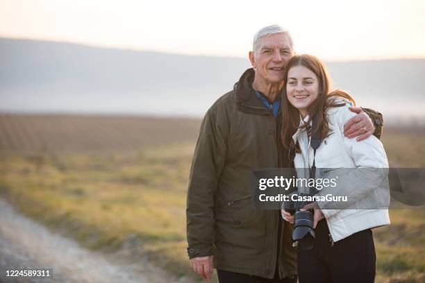 portret van grootvader die kleindochter in openlucht in landelijke scène omhelst - legacy stockfoto's en -beelden
