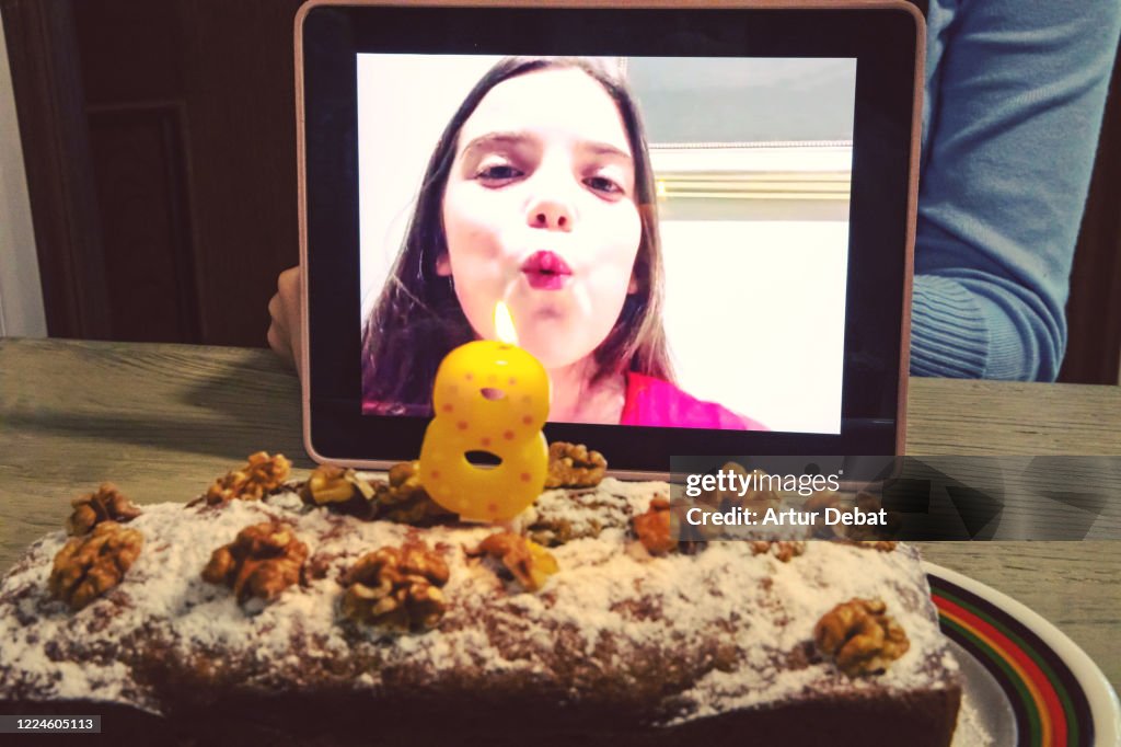 Celebrating creative birthday of child using video call with digital tablet during Covid-19 quarantine blowing candle.