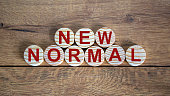 NEW NORMAL word on wooden alphabet circles. New normal concept. Beautiful wooden background.